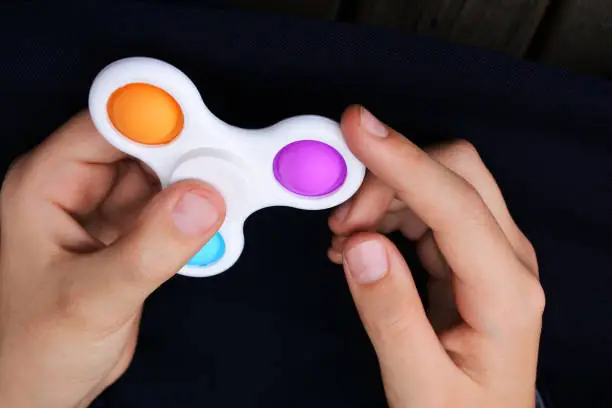 Photo of Hands of a child playing withpop it fidget spinner toy