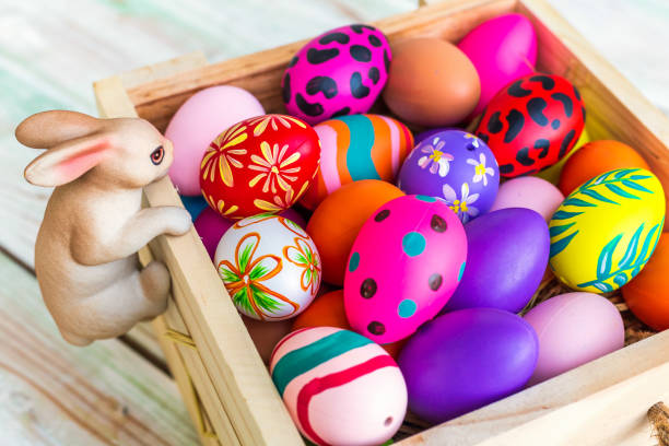 istock Easter holiday concept,Garden ornaments rabbit statues with Colorful Easter eggs in basket on white pastel color rustic wood background with space. 1320755966