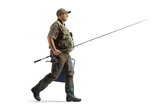 Full length profile shot of a mature fisherman in a uniform walking with a fishing rod isolated on white background