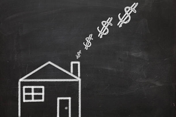 A drawing on a chalkboard of a house with dollar signs rising up from its chimney.  Implies that heating a home costs money.