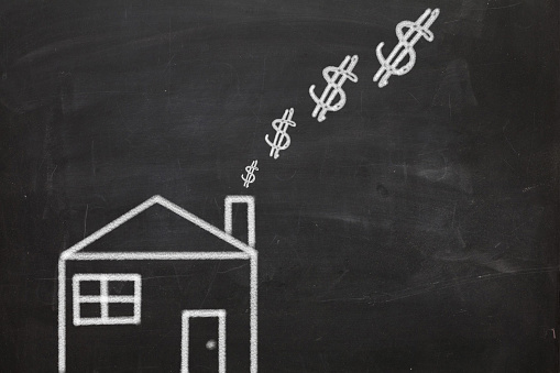 A drawing on a chalkboard of a house with dollar signs rising up from its chimney.  Implies that heating a home costs money.