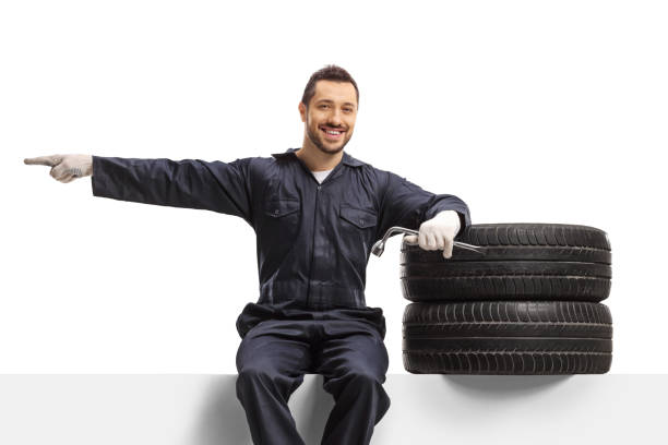 istock Auto mechanic worker sitting on a panel with tires and pointing to the side 1320769062