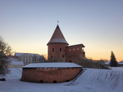 Historic old red tower in a snow covered area under a clear sky in the early evening in Kaunas in Lithuania December 31,2015