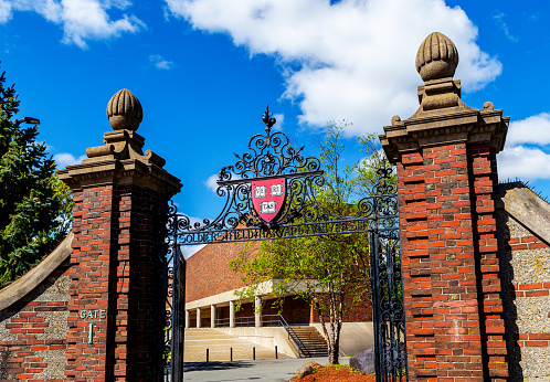 Boston, Massachusetts, USA - May 12, 2021: Gate 1, the Newell Gate pedestrian entrance to Harvard University's Soldiers Field Athletic Area. Blodgett Pool building in background. Atop the gate is the Harvard crest, logo, with three books and the word Veritas (Truth).