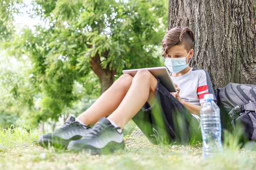 Child wearing protective mask when reading e-book at the park