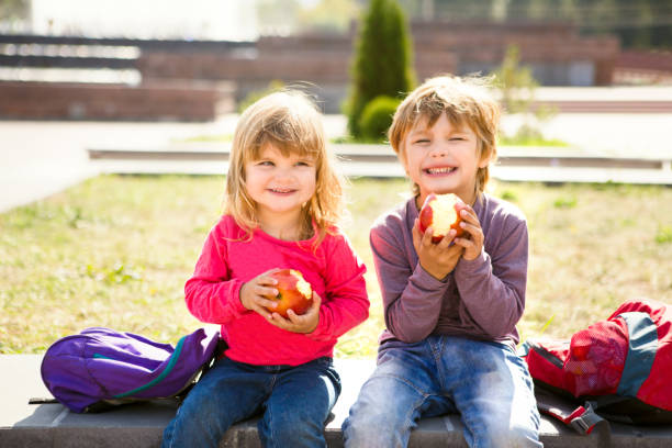 屋外でリンゴを食べるかわいい小学生。子供の頃、健康的な学校の朝食のコンセプト。 - child eating apple fruit ストックフォトと画像