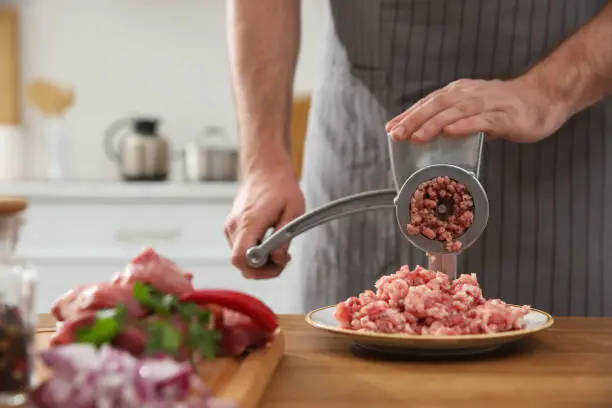 Man using hand meat grinder in kitchen, closeup