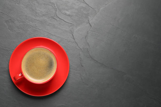 istock Aromatic coffee in red cup on black background, top view. Space for text 1320773496
