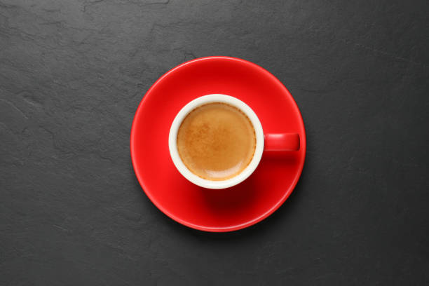 istock Aromatic coffee in red cup on black background, top view 1320774368