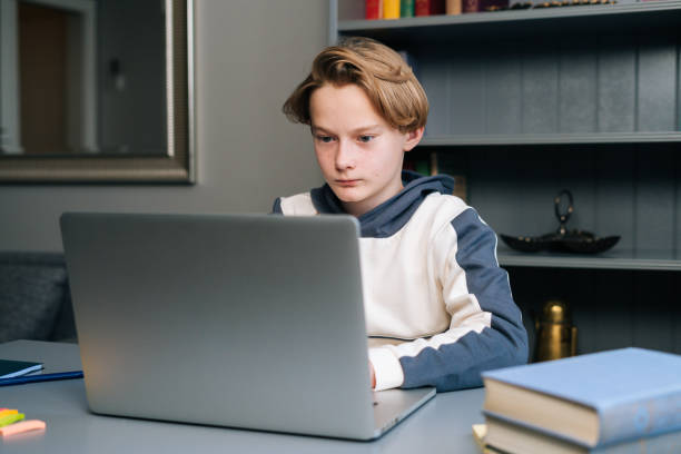 istock Portrait of cute pupil boy using typing laptop computer doing online lesson via Internet at desk, selective focus. 1320776785