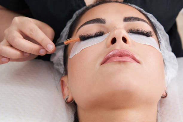 Cosmetologist making eyelash extention and correction using brush stock photo