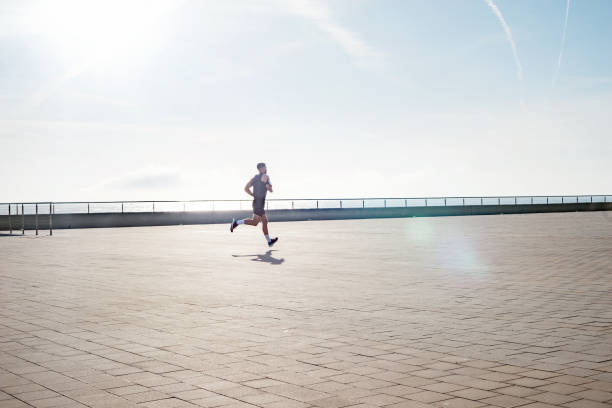 um jovem em forma correndo ao longo da beira-mar. corredor masculino correndo no início da manhã. treinamento de fitness ao ar livre. treino durante o confinamento fora da academia. - crossfit exercising sports training outdoors - fotografias e filmes do acervo