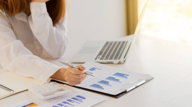 istock A business man studying statistics and holding graph papers by hand an office worker stands near a desk with a laptop and a calculator 1320782158