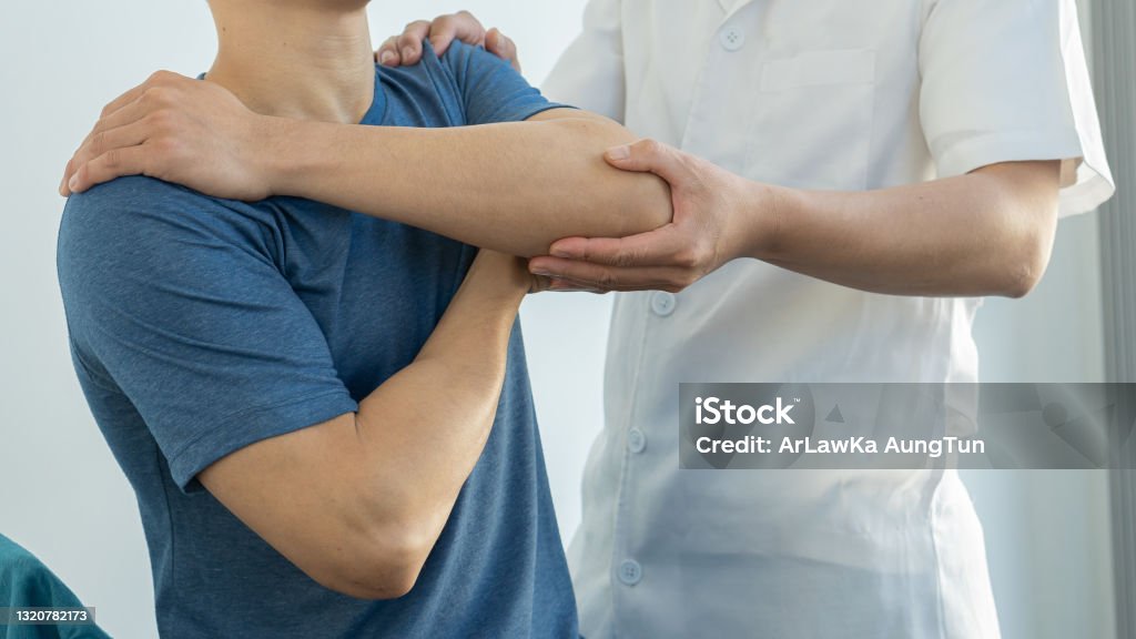 A young man has pain in his elbow on his side due to tennis elbow syndrome. Relief by supporters with a doctor to look at. Physical Therapy Stock Photo