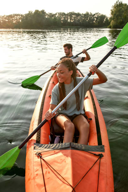 abenteuerlustige junge freundin paddelt kajak auf einem fluss zusammen mit ihrem freund an einem sommernachmittag - sports team sport rowing teamwork rafting stock-fotos und bilder