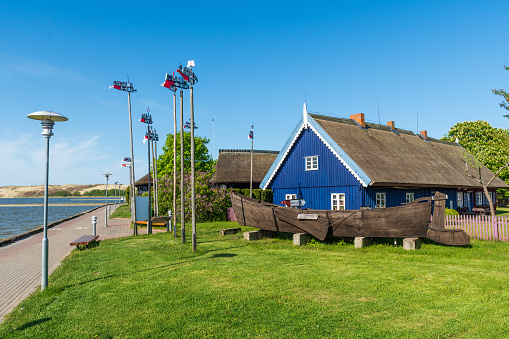 Nida, Lithuania - May 23 2021: Fisherman's museum. Beautiful old Lithuanian traditional wooden blue houses with thatched roof and old boat of the Curonian Spit in Nida fishermen's village, Lithuania