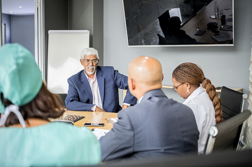 Senior hospital administrator talks with medical staff in boardroom meeting. Hospital administrator discussing important policy issues with medical staff.