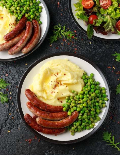 schweinefleisch chipolata würstchen mit hausgemachten kartoffelpüree und grünen erbsen - weenies stock-fotos und bilder