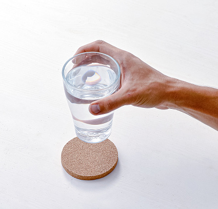 a view of a human hand put glass of water on a cork coaster