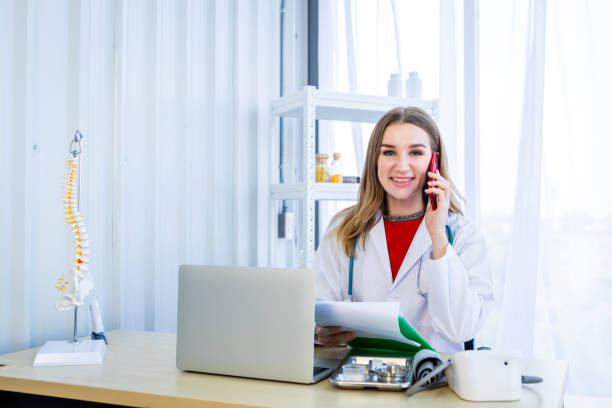 istock female doctor hold pick up Smartphone with stethoscope working with laptop computer and writing on paperwork on wooden table in Hospital background 1320793589