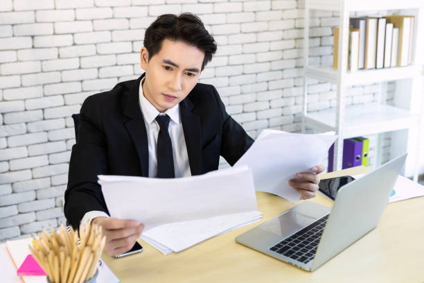 istock asian young businessman have stressed see a the document  business plan and laptop computer on wooden table after business losses In the office room background. 1320796904