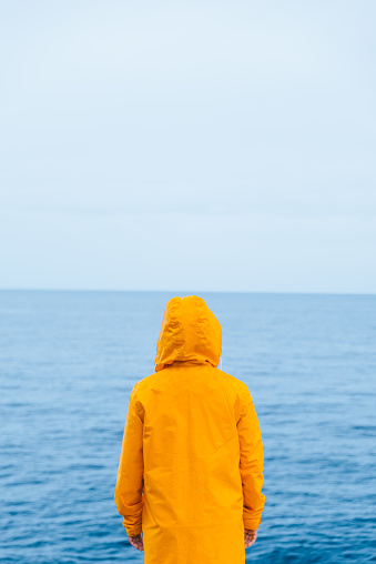 woman in yellow raincoat at sea beach cliff at storm rainy weather. summer vacation. travel concept. hiking
