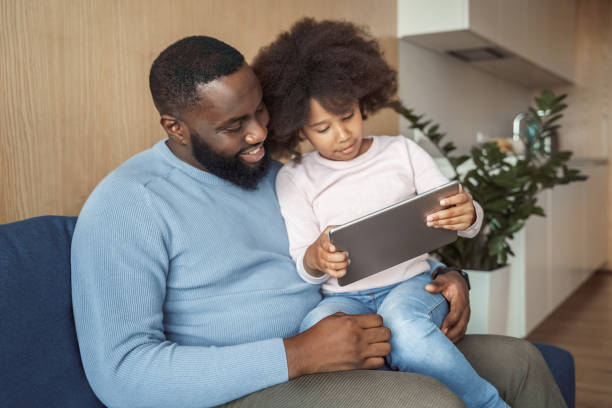 istock Smiling dad and daughter sitting on couch using digital tablet at home 1320800633