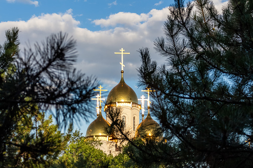 View of The Church of All Saints through pine tree branches in Mamayev Hill War Memorial at sunset in Volgograd city, Russia. Blue sky with grey cloud. Russian orthodox theme.