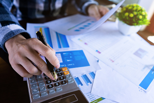 Cierre el hombre de negocios usando la calculadora y la lectura de documentos en papel sobre datos comerciales, documentos de contabilidad, gráficos de la empresa de ganancias. photo