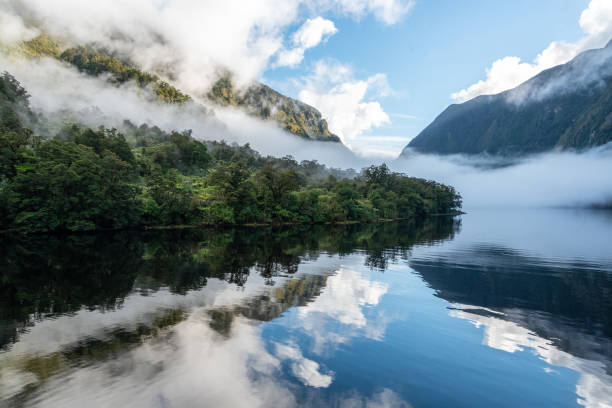 un nouveau matin à l’aube à doutful sound, des nuages suspendus bas dans les montagnes, parc national de fiordland, nouvelle-zélande - sunrise hill sea sun photos et images de collection