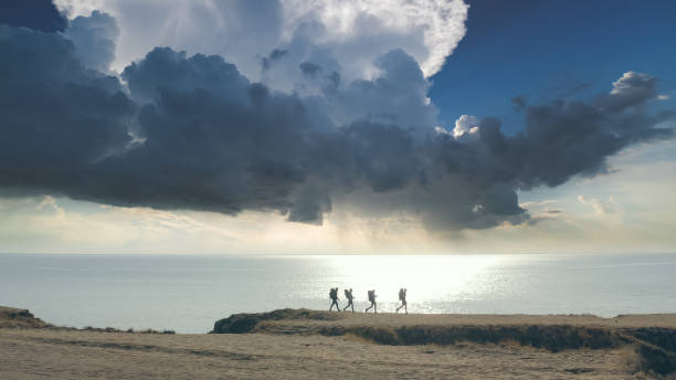 группа из четырех человек идет к краю горы у моря - hiking coastline waters edge sunny стоковые фото и изображения