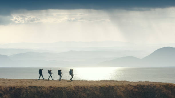 the group of four people walking to the mountain edge near the sea - hiking coastline waters edge sunny imagens e fotografias de stock