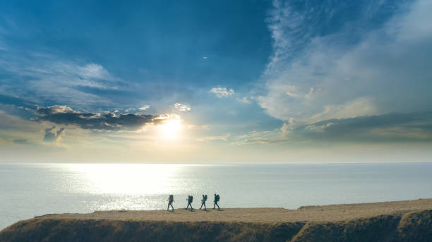 the group of four people walking to the mountain edge near the sea - hiking coastline waters edge sunny imagens e fotografias de stock