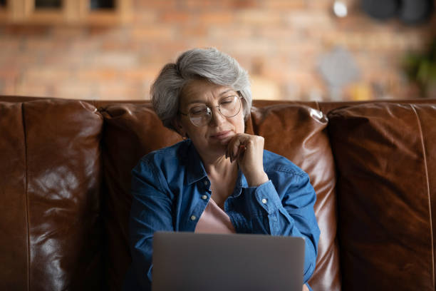 istock Thoughtful mature woman sitting on sofa with laptop 1320817091