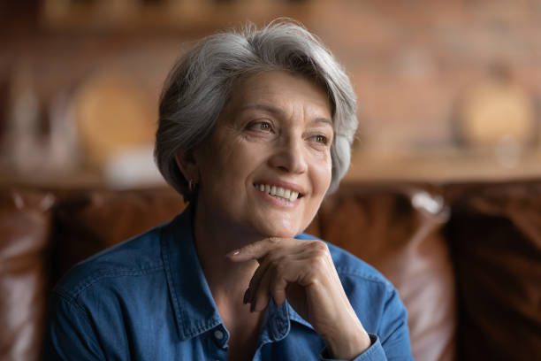 istock Elderly hoary female sitting on couch smiling looking away 1320817097