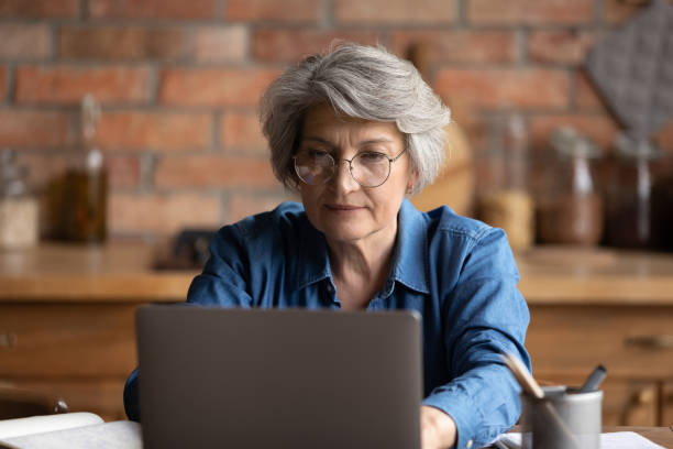 istock Serious woman working on laptop seated at table in kitchen 1320817120