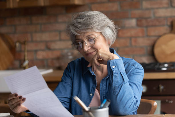 istock Elderly woman sit at table in kitchen reading paper document 1320817127