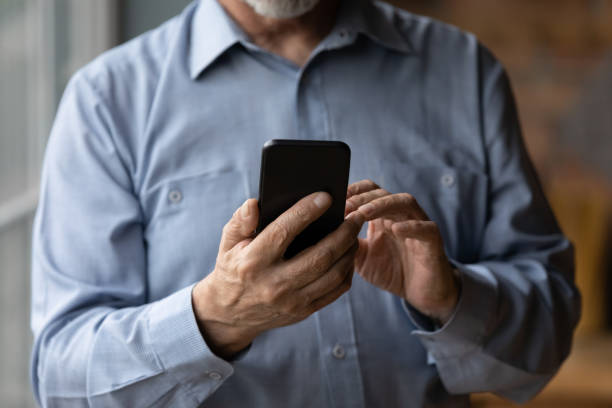 istock Midsection closeup view aged man standing indoor holding smartphone device 1320817177