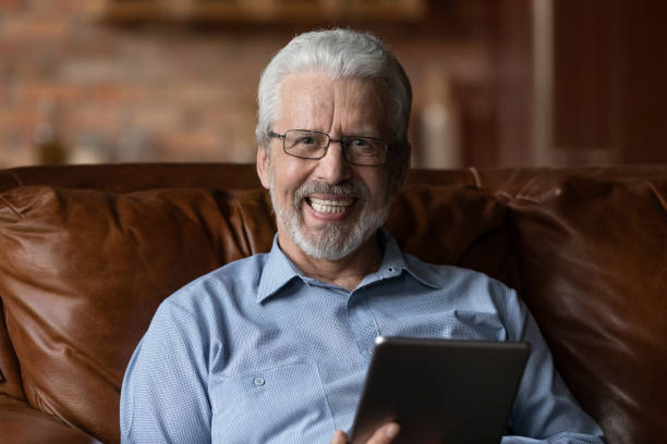 istock Relaxed older man sit on sofa at home with tablet 1320817180