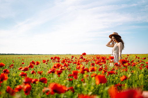 Young woman walking in amazing poppy field. Summertime. Beautiful woman posing in the blooming poppy field. Nature, vacation, relax and lifestyle.