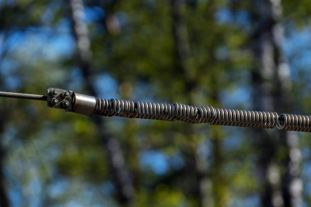 A steel spring is attached to a metal cable. Horizontally. Fixed with a locking device. Four bolts.