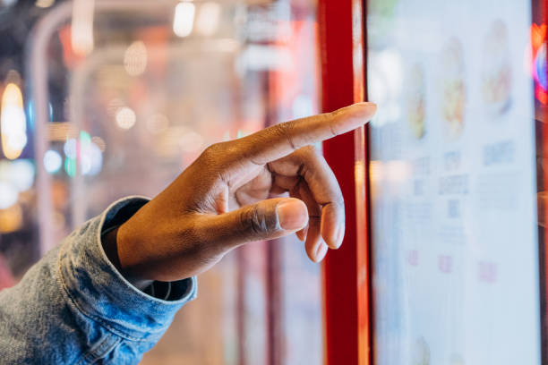 A close-up finger selects a burger on an electronic touch screen at a self-service checkout at a fast food restaurant