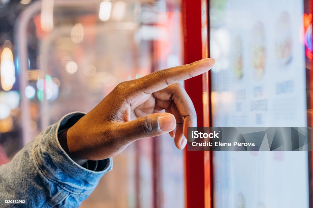 A close-up finger selects a burger on an electronic touch screen at a self-service checkout at a fast food restaurant A close-up African finger selects a burger on an electronic touch screen at a self-service checkout at a fast food restaurant Touch Screen Stock Photo
