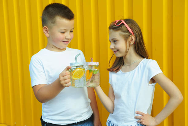 little friends in white t-shirts hold summer cold cocktails with orange and mint on a yellow background - drinking little girls women wine imagens e fotografias de stock