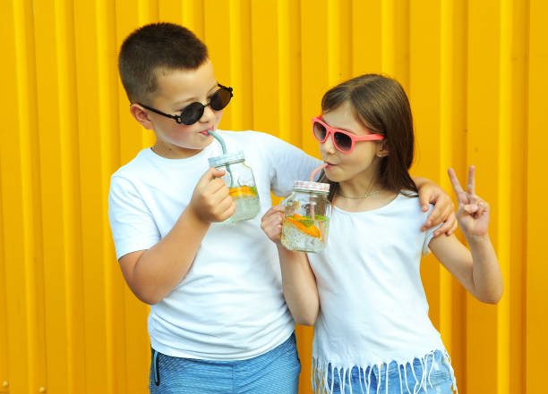 little friends in white t-shirts hold summer cold cocktails with orange and mint on a yellow background - drinking little girls women wine imagens e fotografias de stock