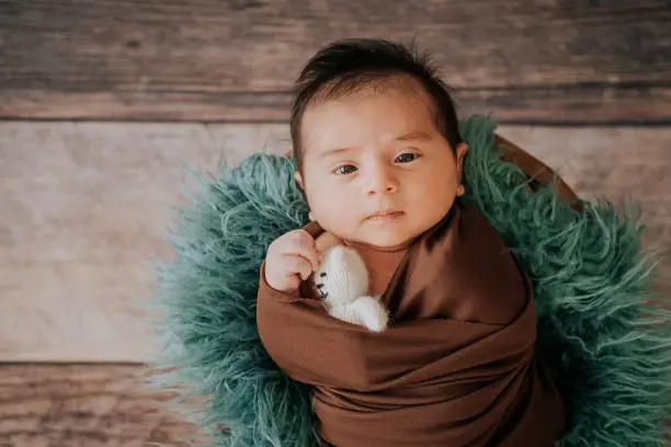 Photo of Little baby boy with knitted hat in a basket, happily smiling and looking at camera, isolated studio shot