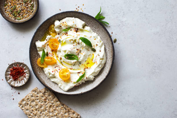 Homemade yogurt cheese (labneh) with tomatoes, seeds and olive oil Homemade yogurt cheese (labneh) with tomatoes, seeds and olive oil in rustic plate on gray stone background close up. Flat lay greek yogurt photos stock pictures, royalty-free photos & images