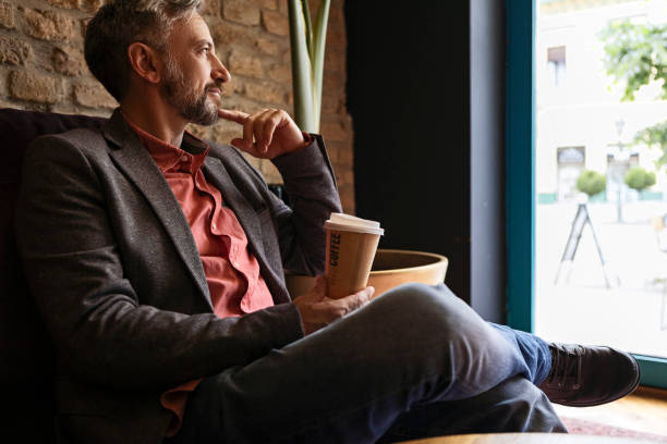 istock Businessman holding cup of coffee sitting looking through window thinking 1320840081