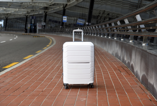 White suitcase stands on the sidewalk at the airport