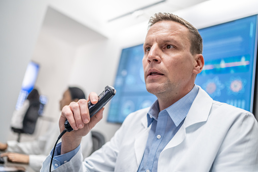 Low angle view of Caucasian doctor recording report on professional dictating device. Examination at specialized medical clinic, diagnosis and healthcare concept.